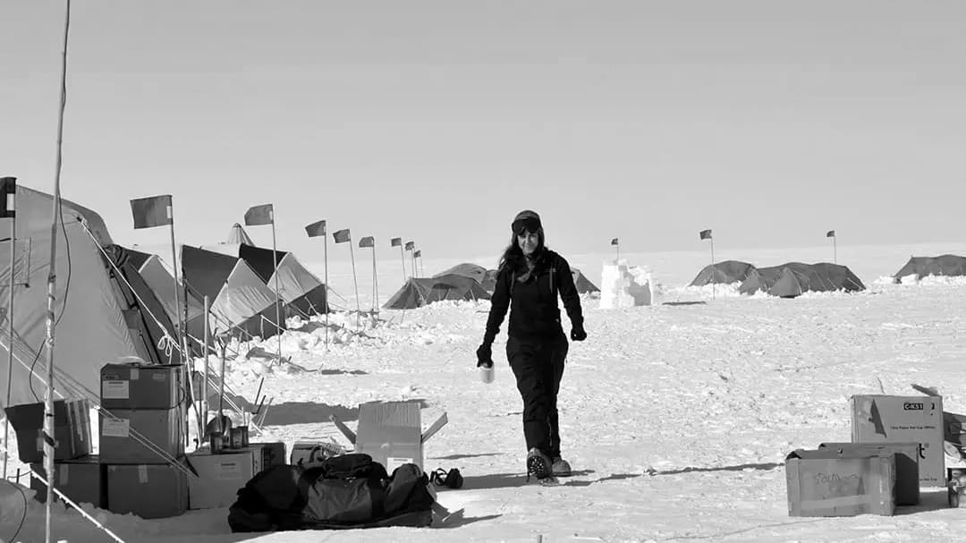 Person walking through snowy expedition camp with tents.