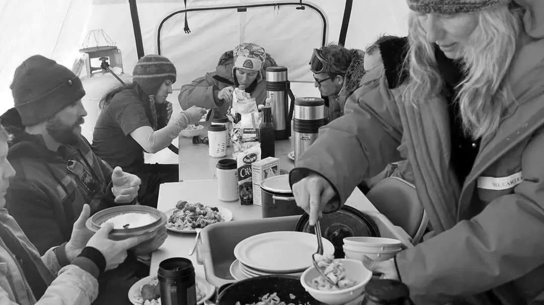 Group dining in a tent during winter expedition.