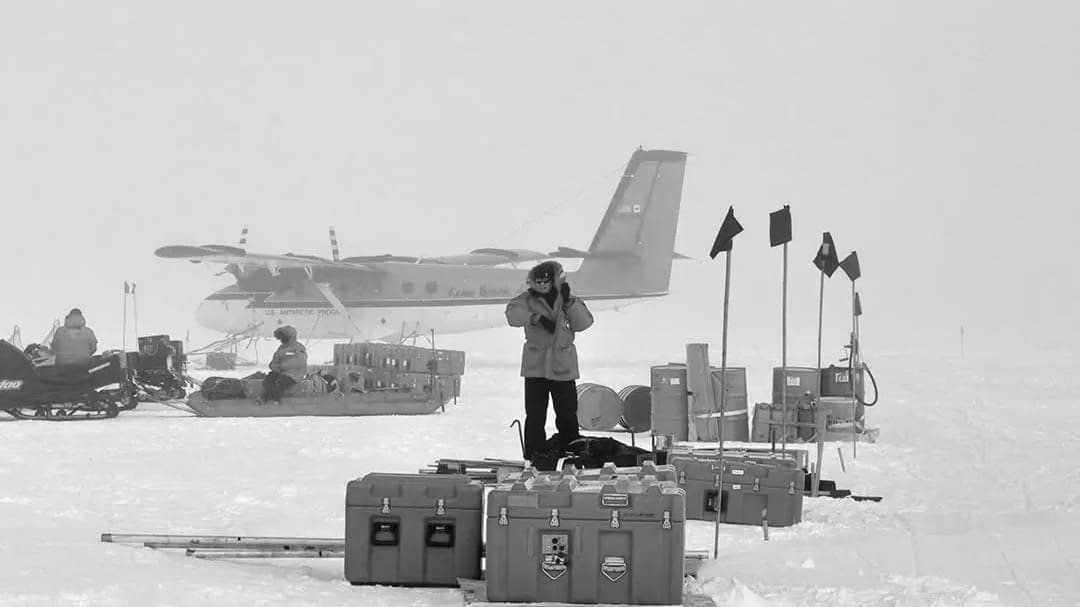 Researchers unloading equipment near plane in snowy Arctic.