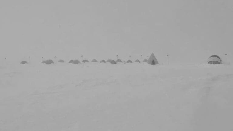 Snowy landscape with distant tents and flags.