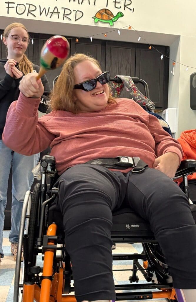 Smiling woman in wheelchair shaking a maraca
